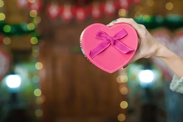 La mano de la mujer sosteniendo la caja rosa en forma de corazón — Foto de Stock