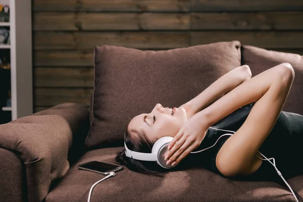 Dívka s mikrofonem leží na pohovce a poslouchat hudbu — Stock fotografie