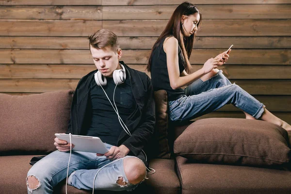 Adolescentes enamorados sentados en la cama con teléfono inteligente, auriculares y tabletas — Foto de Stock
