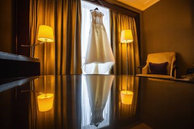 Otel odasında pencere yakınındaki bir askı asılı gelinlik