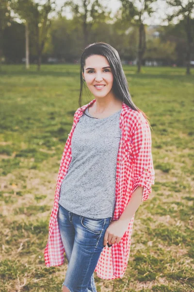 Hipster woman in red shirt and ripped jeans posing in park — Stock Photo, Image