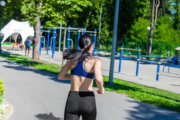 Mujer deportiva corriendo por el camino cerca del parque infantil deportivo — Foto de Stock