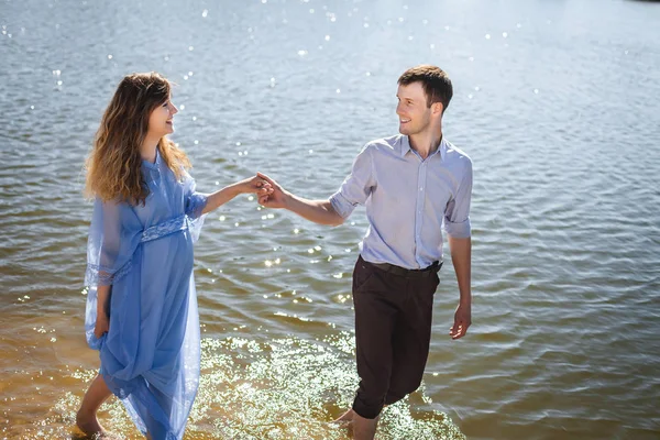 Guy and pregnant woman walking on water along river shore holding hands together — Stock Photo, Image