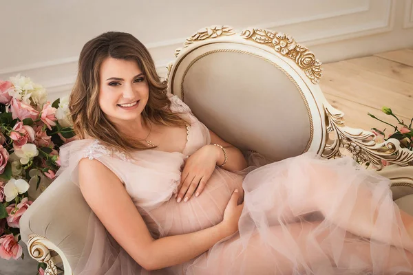 Young happy future mother lying on luxury armchair and hugging belly — Stock Photo, Image