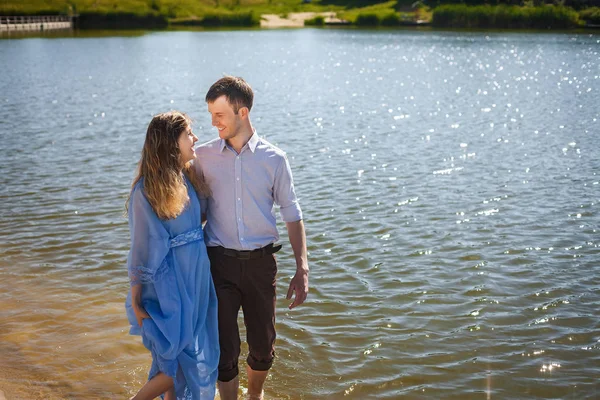 Man and pregnant girl walking on water along river shore holding hands together — Stock Photo, Image