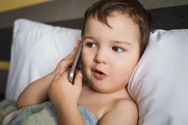 Liten pojke prata mobiltelefon ligger på sängen i morgon — Stockfoto