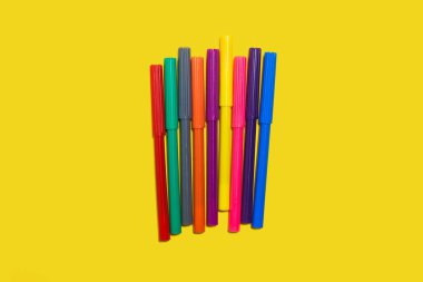 Sarı arka planda duran renkli keçeli kalemler.