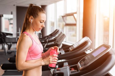 Koşu bandında elinde protein kokteyliyle koşan bir kız.