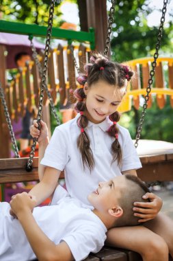 Kız kardeş bacaklarının üzerinde uzanan tatlı çocuk bankta oturuyor.