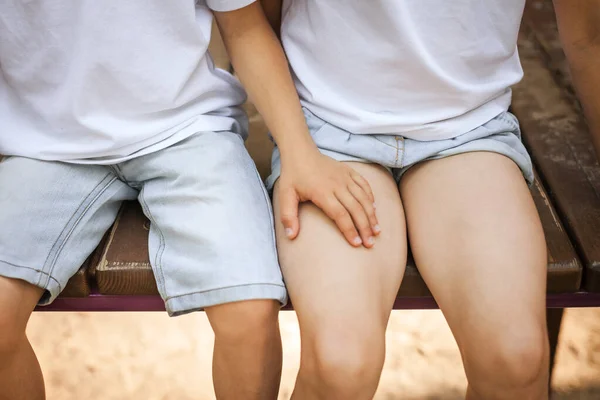 Garçons main sur filles jambes assis sur le banc — Photo