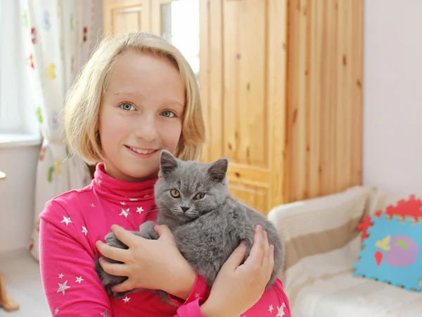 Chica feliz sostiene un pequeño gatito en la habitación de los niños — Foto de Stock