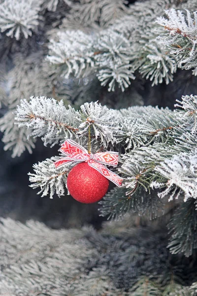 Glänzende Weihnachtskugel mit Schleife an einem schneebedeckten Baum. Weihnachtlicher Hintergrund. — Stockfoto