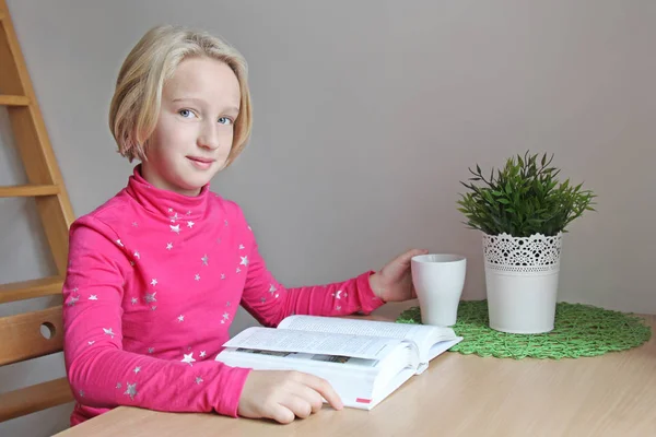 Mädchen im Schulalter liest ein Buch, während sie an einem Tisch in einer Wohnung sitzt Stockfoto
