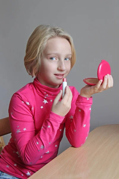 Mooi blonde meisje van de school-leeftijd schildert haar lippen met lippenstift kind, ze doet make-up — Stockfoto