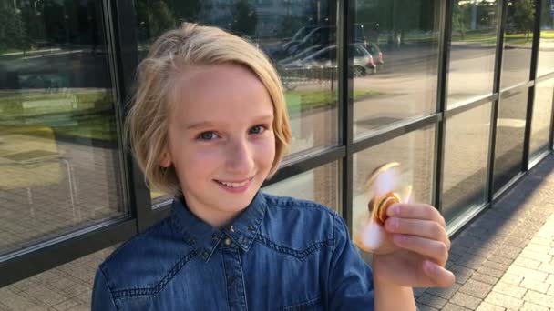 Mooie vrolijke school meisje speelt met een gouden fidget spinner. Een populaire trendy speelgoed. — Stockvideo