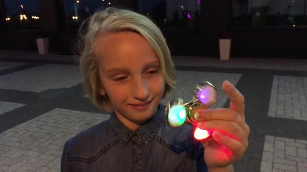 Glada Skolflicka som leker med en lysande fidget spinner, kväll utomhus. En populär trendiga leksak. — Stockvideo