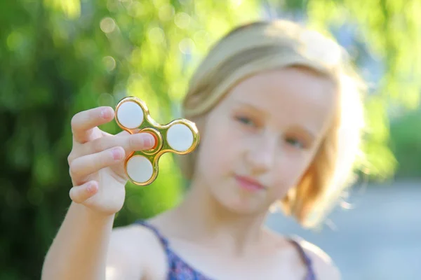 School oud meisje speelt met een gouden fidget spinner. Een populaire trendy speelgoed. — Stockfoto