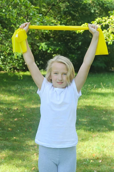 Vackra skolan åldern kid flicka att idrotta med latex band utomhus i parken — Stockfoto