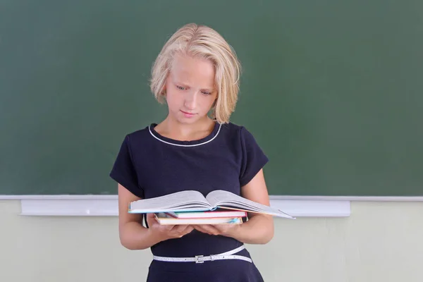 Очаровательная блондинка читает книгу в классе возле доски. Возвращение в школу . — стоковое фото