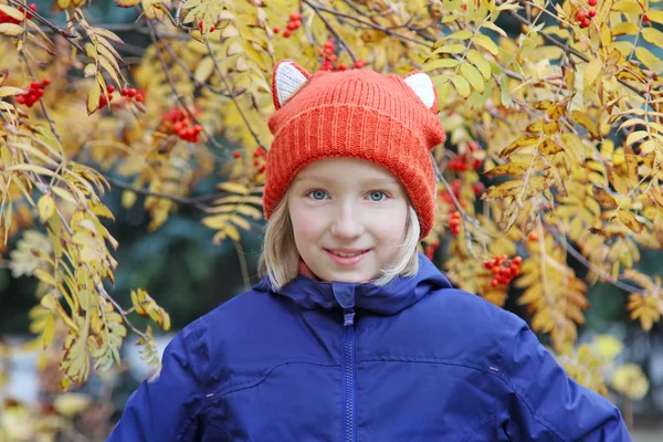 Rozkošné dítě dívka s úsměvem, dítě je oblečená v legrační pletené teplé čepice s ušima, vypadá jako liška. Podzim, portrét venku. — Stock fotografie