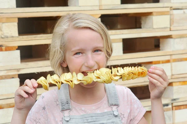 Ragazza che mangia patatine su un bastone. Cibo spazzatura, cibo di strada, spuntino a piedi . Foto Stock