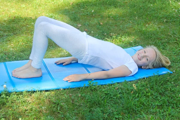 Güzel sarışın varoluş kız ışık giyim pratik yoga mat parkta. Sağlıklı bir yaşam tarzı. Açık havada egzersiz. 