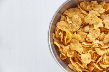 Boyalı Beyaz ahşap zemin üzerinde metal bir kase mısır gevreği. Yazı için boş alan.