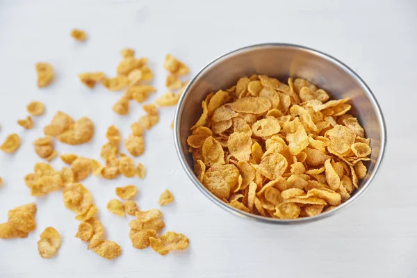 Cornflakes in einer Metallschale auf einem bemalten weißen Holzgrund. Cornflakes auf Holztisch verstreut. — Stockfoto