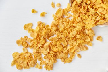 Plaser ile boyalı Beyaz ahşap zemin üzerinde metal bir kase mısır gevreği. Ahşap bir masa üzerinde dağınık Mısır gevreği.