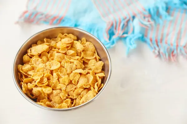 Cornflakes in einer Metallschale auf einem bemalten weißen Holzgrund. Komposition mit einem Geschirrtuch. — Stockfoto