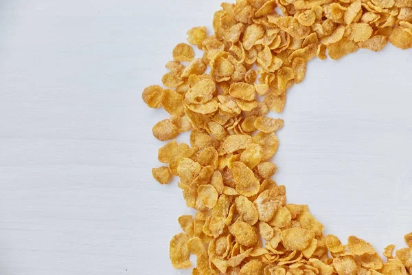 Round frame lined with corn flakes. Cornflakes scattered on a wooden table.