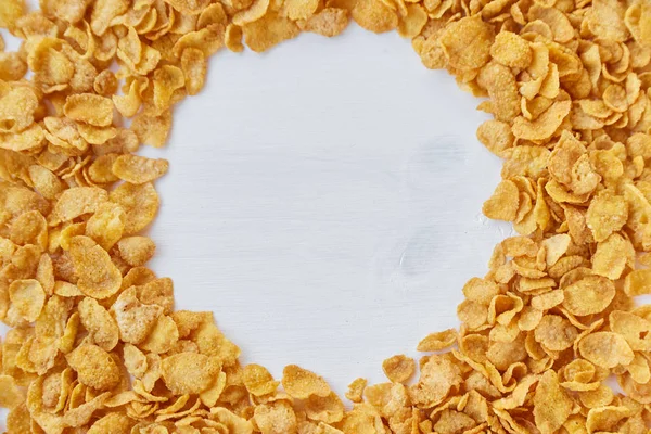 Runder Rahmen, ausgekleidet mit Cornflakes. Cornflakes auf Holztisch verstreut. — Stockfoto