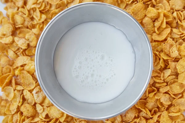 Round frame with metal bowl with milk lined with corn flakes. Cornflakes scattered on a wooden table.