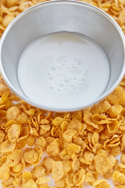 Metallschale mit Milch auf einem bemalten weißen Holzgrund. Cornflakes auf Holztisch verstreut. — Stockfoto