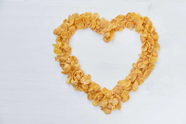 Cornflakes on a painted white wooden background. The symbol of the heart is laid out of cornflakes. Stock Picture