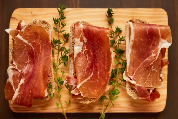 Sandwiches made from hand-made rye bread and thin chopped fresh bacon. Fresh green thyme on a wooden board. Succulend bacon on a wooden table. — Stock Photo, Image