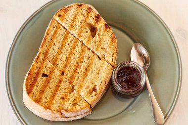 Beyaz ahşap masada kiraz reçeli ile tost. Gri parlak plaka üzerinde kızarmış ekmek.