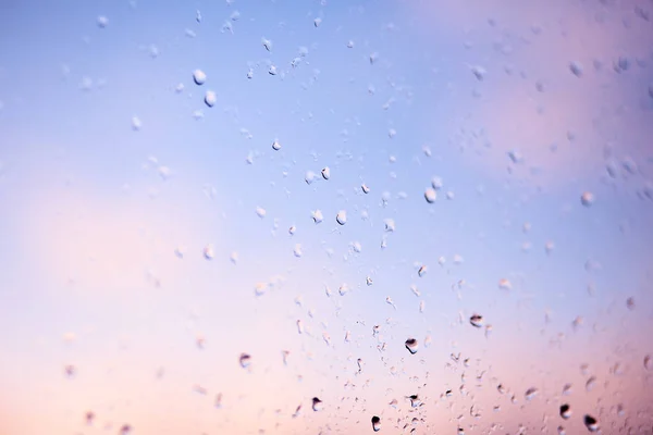 Gocce di pioggia sul parabrezza dell'auto la mattina presto. Vetro trasparente dopo la pioggia, foto astratta mignolo. Texture di vetro con gocce di pioggia sparse e uno sfondo sfocato nel crepuscolo . — Foto Stock