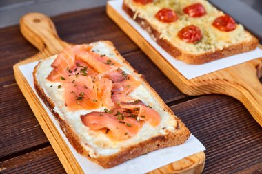 Kurutulmuş domates ve peynir ve somon bir ışık kesme tahtası ve kahverengi ahşap bir masa üzerinde pişmiş sandviç eritilmiş peynir ve güneş ile kümesi. Doğal ışıkla fotoğrafı.