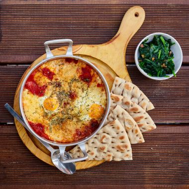 Domates, peynir ve ev yapımı ince lavaş ve ahşap bir kahverengi masa üzerinde sulu yeşillik ile kulplu bir alüminyum tava içinde baharatlar ile omlet. Doğal ışık altında fotoğraf çekildi.