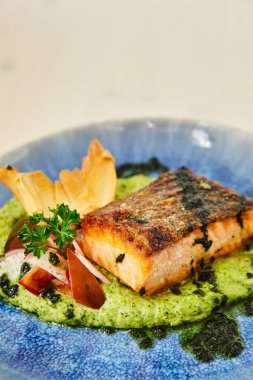 Büyük sulu kavrulmuş yağlı parça somon Steak turp, maydanoz, kişniş ile dekore edilmiş ve hamur fırında sebze püresi, bir yastık üzerinde. Balık yemek beyaz ahşap bir masa üzerinde güzel bir mavi plaka.