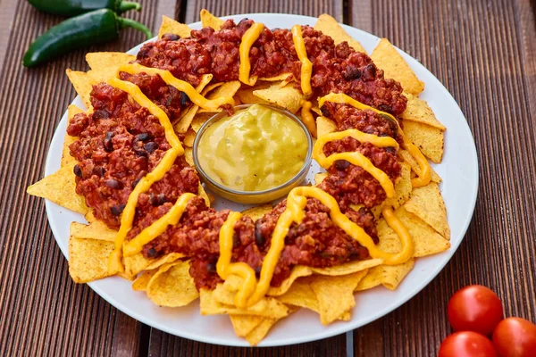 National Mexican and Chilean dish on a wooden table. Homemade potato chips with tomato sauce, beans and minced meat. Mustard sauce in the middle of the dish. Decorated with green peppers and tomatoes. — Stock Photo, Image