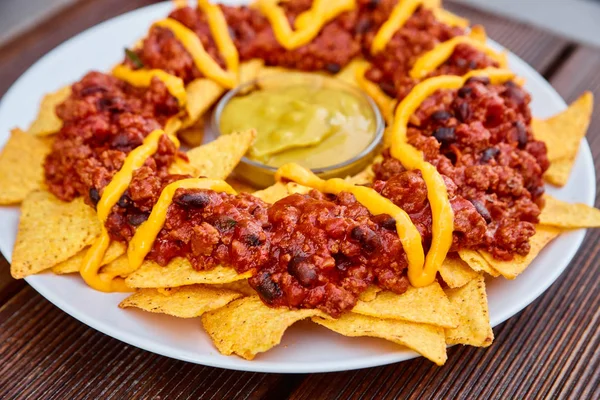 Plato nacional mexicano y chileno sobre una mesa de madera. Patatas fritas caseras con salsa de tomate, frijoles y carne picada. Salsa de mostaza en medio del plato. Decorado con pimientos verdes y tomates . — Foto de Stock