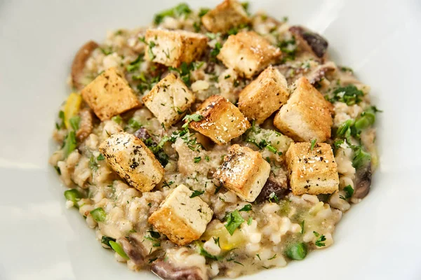 Risotto with mushrooms, toast, parmesan and greens in a large white plate on a dark wooden table. In the background, radish with herbs and spices. National dish of Italy, Italian cuisine.