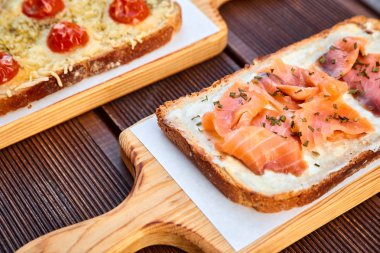 Kurutulmuş domates ve peynir ve somon bir ışık kesme tahtası ve kahverengi ahşap bir masa üzerinde pişmiş sandviç eritilmiş peynir ve güneş ile kümesi. Doğal ışıkla fotoğrafı.