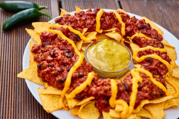 National Mexican and Chilean dish on a wooden table. Homemade potato chips with tomato sauce, beans and minced meat. Mustard sauce in the middle of the dish. Decorated with green peppers and tomatoes. — Stock Photo, Image