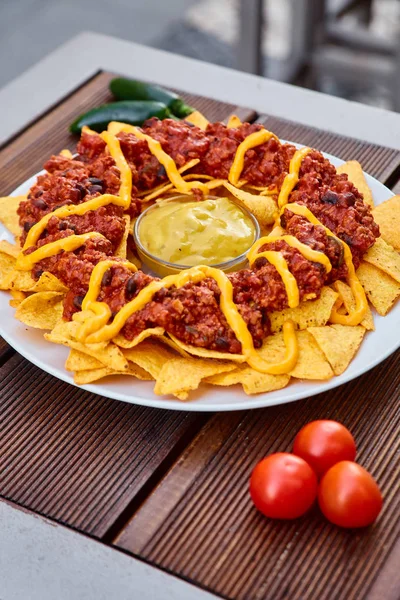 Mexikanisches und chilenisches Nationalgericht auf einem Holztisch. hausgemachte Kartoffelchips mit Tomatensauce, Bohnen und Hackfleisch. Senfsauce in der Mitte des Gerichts. dekoriert mit grünen Paprika und Tomaten. — Stockfoto