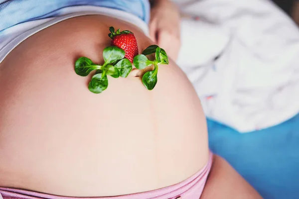 Kırmızı olgun çilek ve yeşil marul hamile bir kadının karnı üzerinde. Gebelikte beslenme sağlıklı bir çocuğun sağlığını garantisidir. Hamile kadınların sağlıklı beslenme kavramı. — Stok fotoğraf