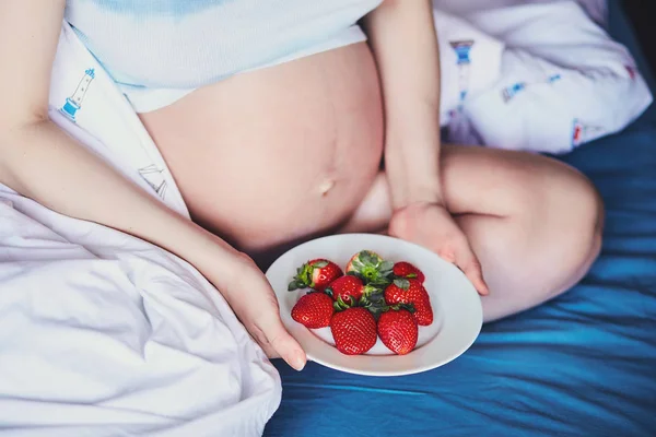 Çekici genç hamile kadın bir yatakta oturur ve olgun çilek yiyor. Gıda mutlu hamile kız, meyve ve sebzeler için dengeli beslenme gelecekteki anne. Başarılı bir gebelik için sağlıklı gıda. — Stok fotoğraf