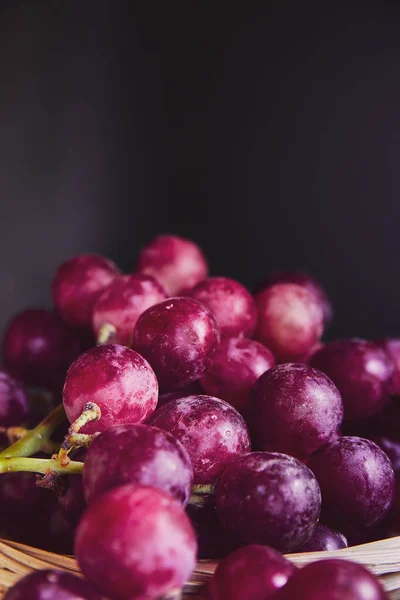 Bunches of purple and red grapes in a wicker basket on a dark background. The harvest of unwashed grapes in a basket. Ecologically bio clean organic grapes from the plantation are collected manually. — Stock Photo, Image